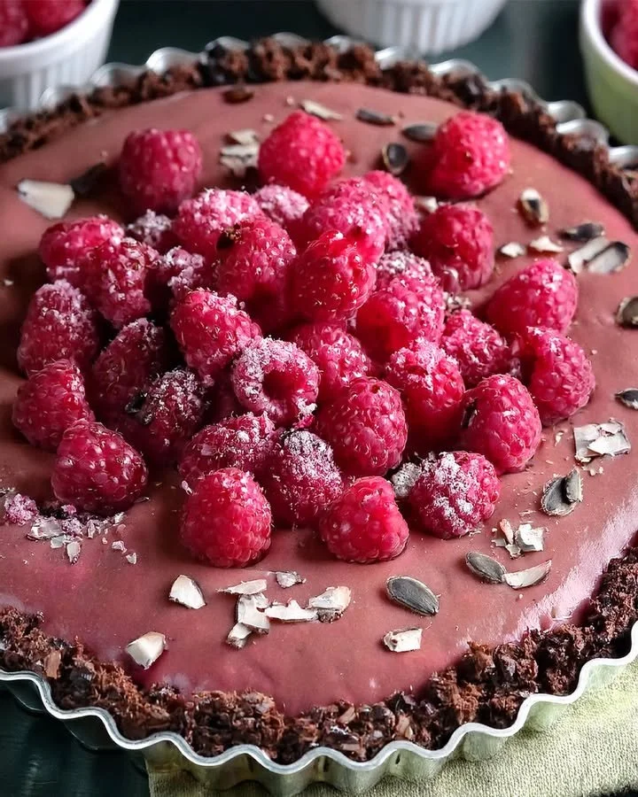 A delicious vegan raspberry chocolate tart garnished with fresh raspberries.