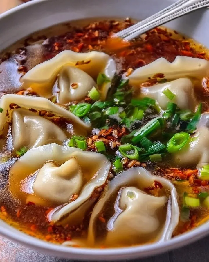 Bowl of delicious wonton soup with fresh herbs and dumplings on a wooden table