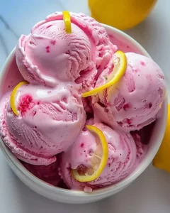 Delicious Rosy Lemonade Ice Cream in a bowl with fresh lemons and vibrant pink color.
