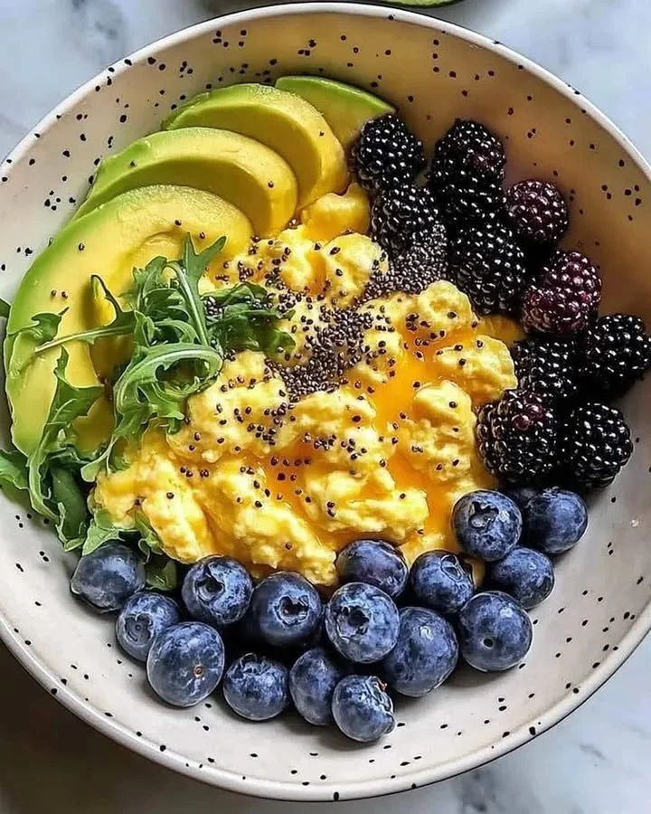 Scrambled eggs avocado berries breakfast bowl served in a vibrant dish.